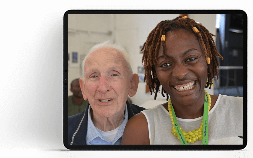 Tablet screen showing a photo of Audrey Mutongi and an older person smiling together at a No.1 Befriending Agency meet up.