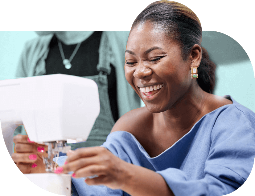 Joyce Addai-Davis, a young Black social entrepreneur smiles, using a sewing machine.