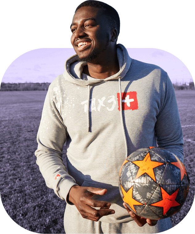 Young Black social entrepreneur Marvin Onu smiles on a grass football pitch, holding an orange patterned football.