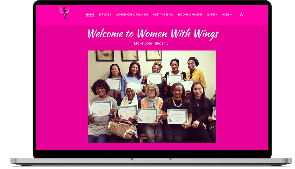 A laptop displaying the pink website homepage of Women With Wings Community Interest Company, which features a photo of an ethnically diverse group of women smiling, holding certificates.